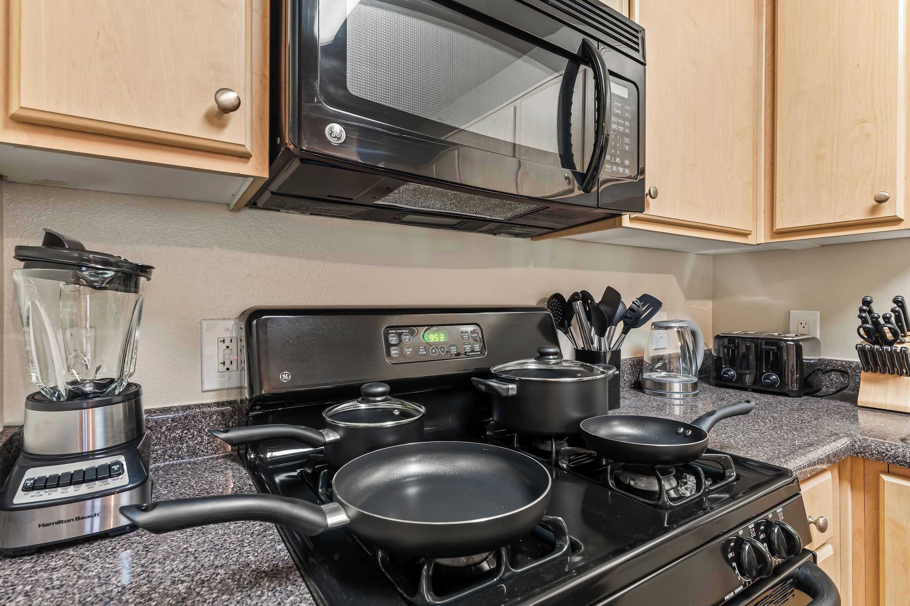 A kitchen with a stove, pots, a blender, and a microwave.