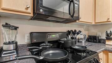 A kitchen with a stove, pots, a blender, and a microwave.