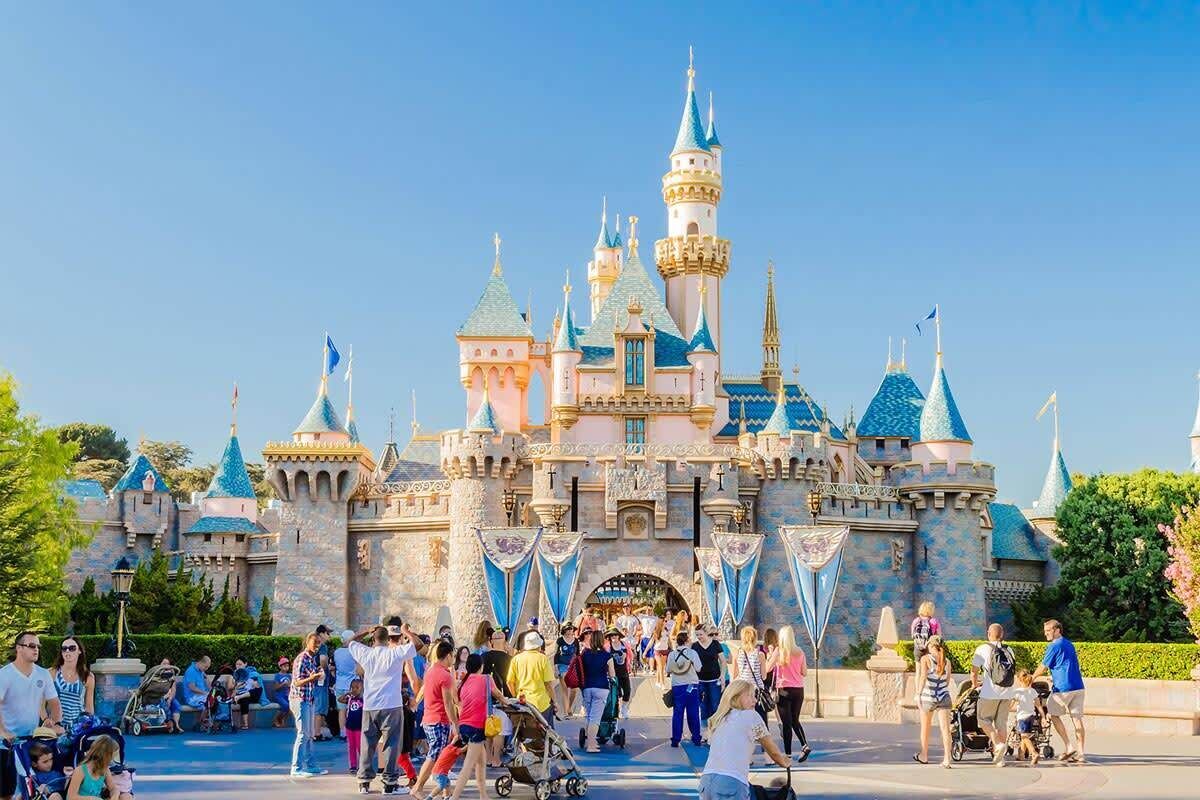 A castle-like structure with multiple towers and flags, surrounded by a crowd of people.