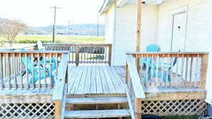 A wooden deck with a lattice railing, a porch, and a view of a grassy field and hills in the background.