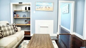 A living room with a white sofa, a coffee table, a fireplace, and a bookshelf.