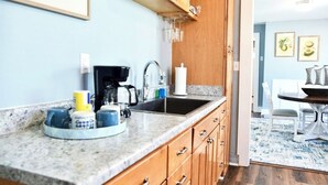 A kitchen with granite countertops, wooden cabinets, and a coffee maker. There is a dining area with a table and chairs visible in the background.