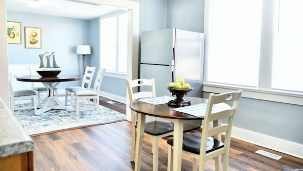 A dining area with a round table, chairs, a bowl of fruit, and a refrigerator.