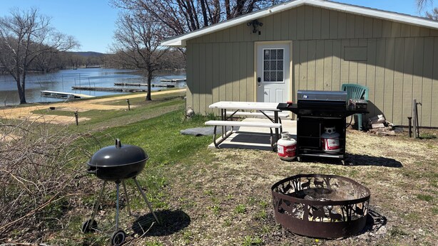 A lakeside cabin with a grill, picnic table, and fire pit.