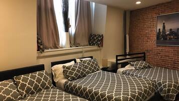 A hotel room with two beds, a window with curtains, a brick wall, and a cityscape painting.