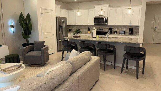 Una cocina moderna con armarios blancos, electrodomésticos de acero inoxidable y una isla central con taburetes de bar.
