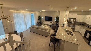 Una cocina moderna con encimera de granito, electrodomésticos de acero inoxidable y una zona de comedor con mesa y sillas blancas.