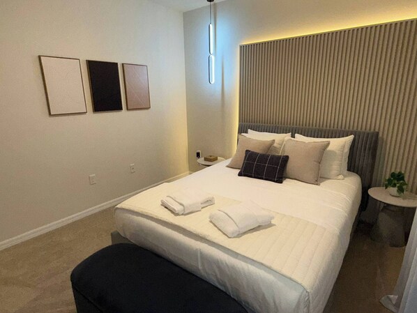 A modern hotel room with a large bed, a bedside table, and a small round table with a plant.