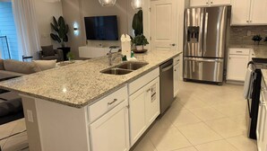 Una cocina moderna con encimeras de granito, electrodomésticos de acero inoxidable e iluminación colgante.