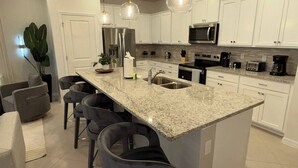 Una cocina moderna con armarios blancos, encimeras de granito, electrodomésticos de acero inoxidable y una isla central con taburetes de bar.