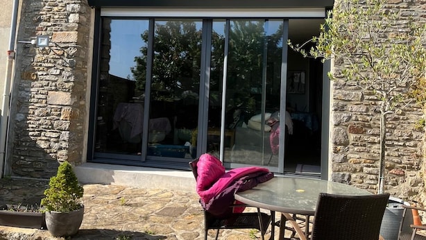 A stone building with a large glass window and a patio area with a table and chairs.