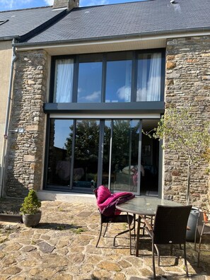 Un bâtiment en pierre doté d’une grande fenêtre en verre et d’un patio avec une table et des chaises.