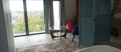 A room with a large window, a round table, a red exercise ball, a blue chair, and a wardrobe.