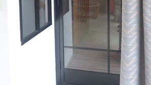 A room with a sliding glass door leading to a balcony, a wooden ceiling, and a patterned curtain.