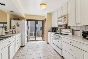 A kitchen with white cabinets, a refrigerator, a stove, and a microwave. There is a balcony visible through the door. - 3 BR/2BA home in So. Bethany (South Bethany)