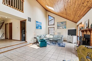 A spacious living area with a high ceiling, a sectional sofa, a television, and a fireplace.