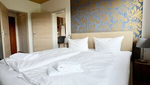 Una cama grande con sábanas blancas y un cabecero, techo de madera y pared con un estampado.