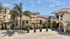 A courtyard with tiled roofs, potted plants, and buildings with balconies. - Puerto Nuevo Villa Olas 2BR 2BA with pool (Centro Turístico El Pescador)