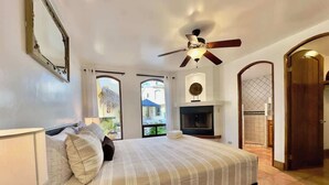 Un dormitorio con una cama grande, ventilador de techo, chimenea y televisor.