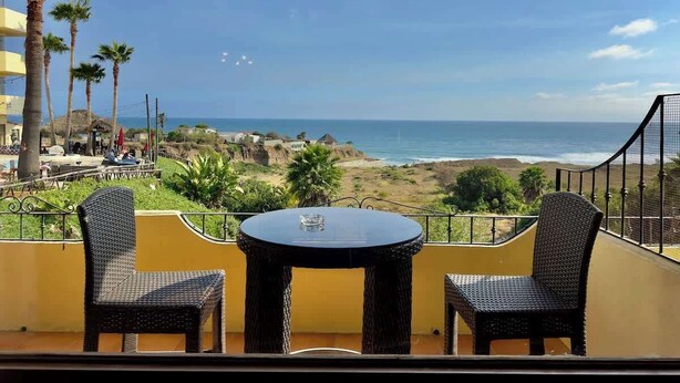 Un balcón con dos sillones de mimbre y una mesa, con vistas a la playa y al océano.