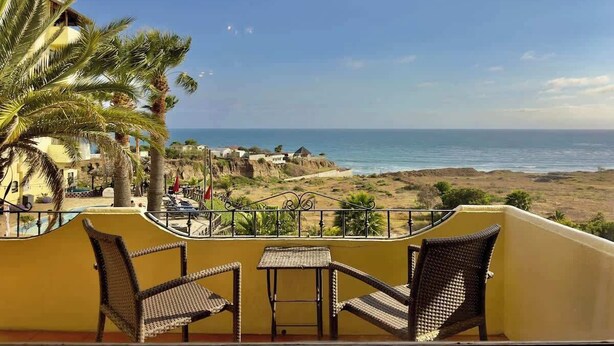 Un balcón con mobiliario de mimbre con vista a una playa y al océano.