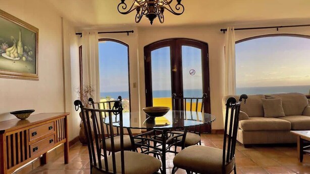 Zona pranzo con un tavolo rotondo e sedie, un divano, e vista sul mare attraverso ampie finestre.