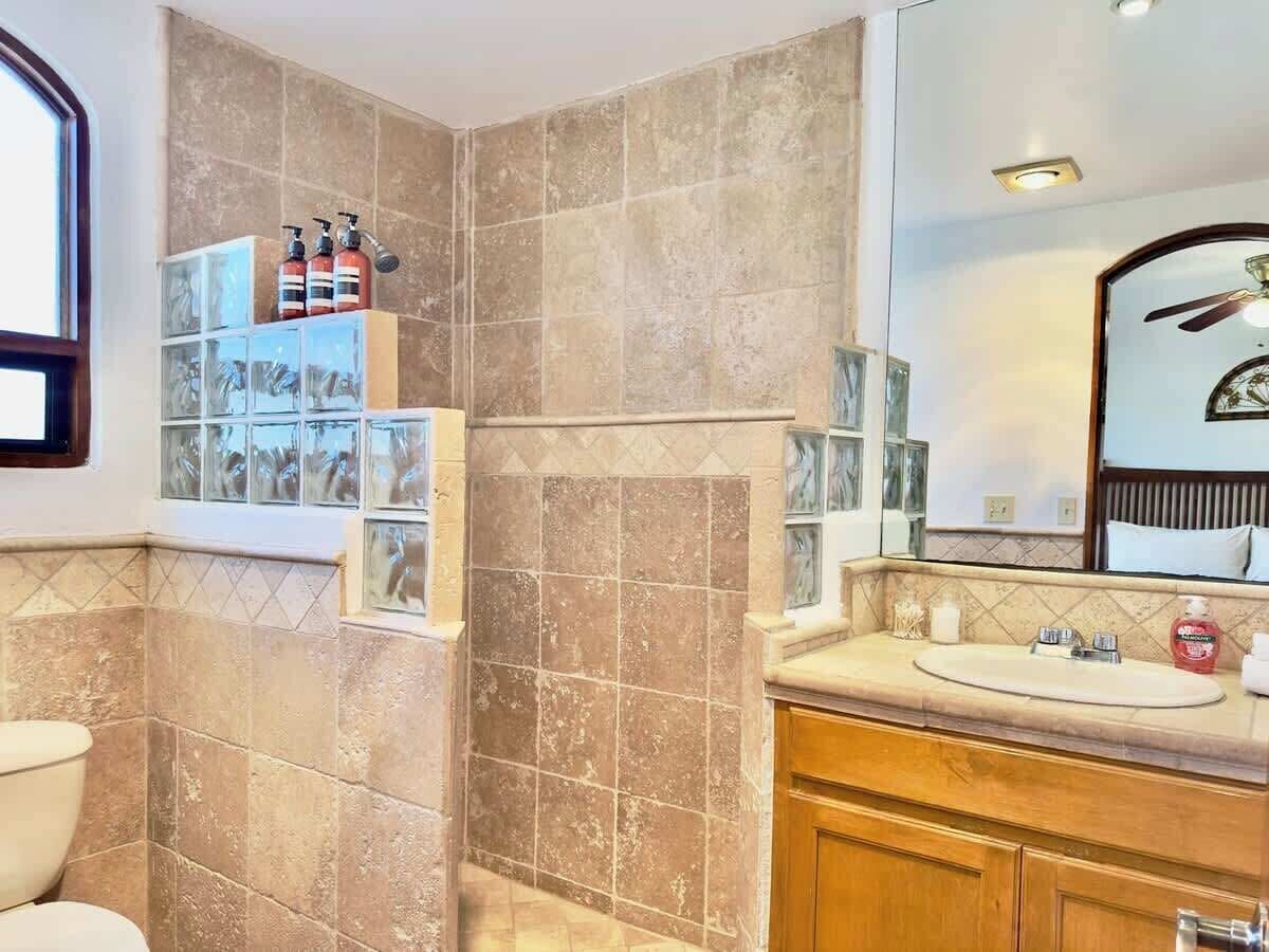 Une salle de bain avec des carreaux de couleur beige, un meuble-lavabo en bois, un miroir et un espace douche.