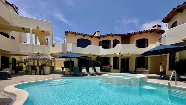A swimming pool with lounge chairs and umbrellas, surrounded by buildings with balconies.