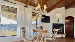 Zona de menjador amb taula i cadires, un lampadari, una llar de foc i un televisor penjat a la paret.
