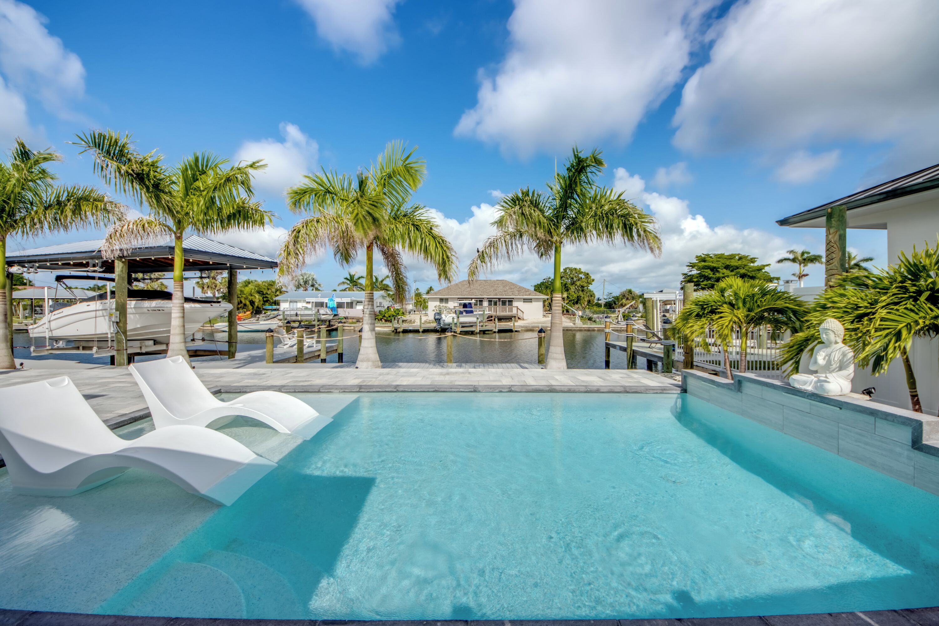 A swimming pool with lounge chairs, palm trees, and a building with a covered area.