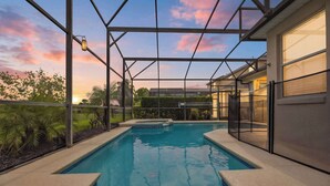 An indoor swimming pool with a glass enclosure, surrounded by a landscaped garden and a building with large windows. - Family Luxury Sunset Oasis - POOL HEATING (Davenport)