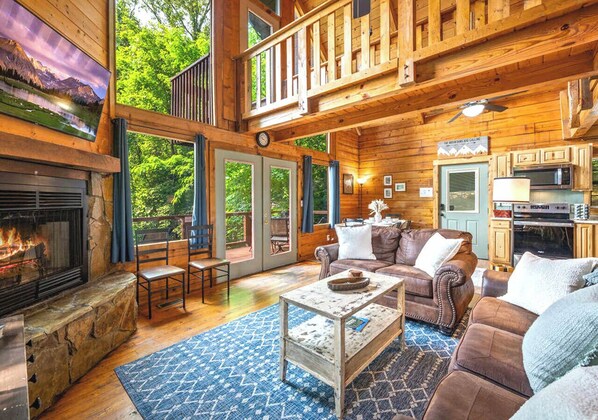 A cabin interior with a fireplace, seating area, and a view of the outdoors.