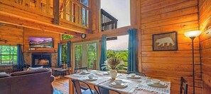 Interior de cabana de madeira com lareira, mesa de jantar posta e televisão.