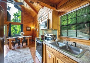 A wooden cabin interior with a kitchen, dining area, and large windows.