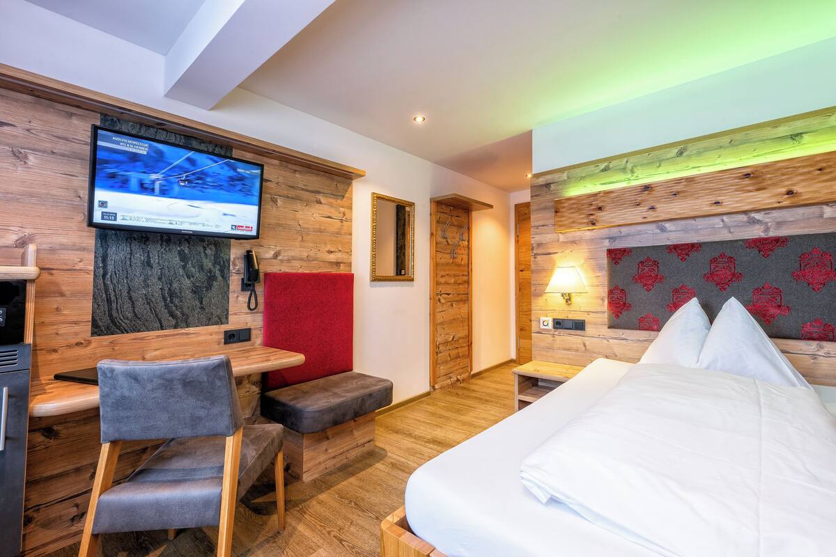 Ein Hotelzimmer mit einem Bett, einem Schreibtisch mit Stuhl, einem an der Wand befestigten Fernseher und einer roten Akzentwand.
