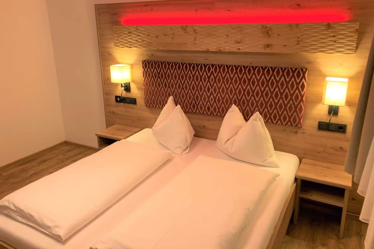 Ein Hotelzimmer mit einem hölzernen Kopfteil, zwei Nachttischen und zwei Wandlampen.