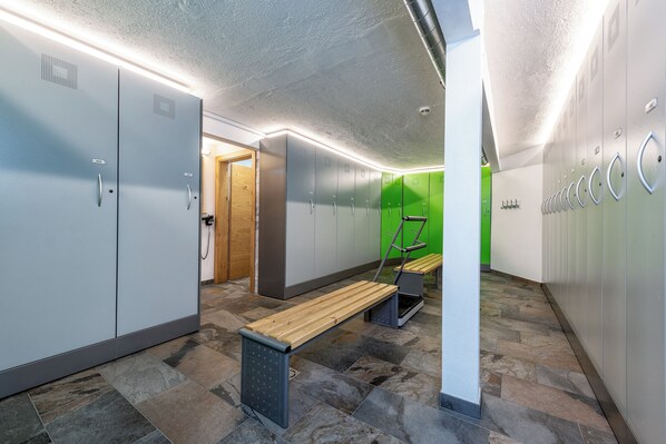 Un vestuario con taquillas grises, un banco de madera y una pared verde.