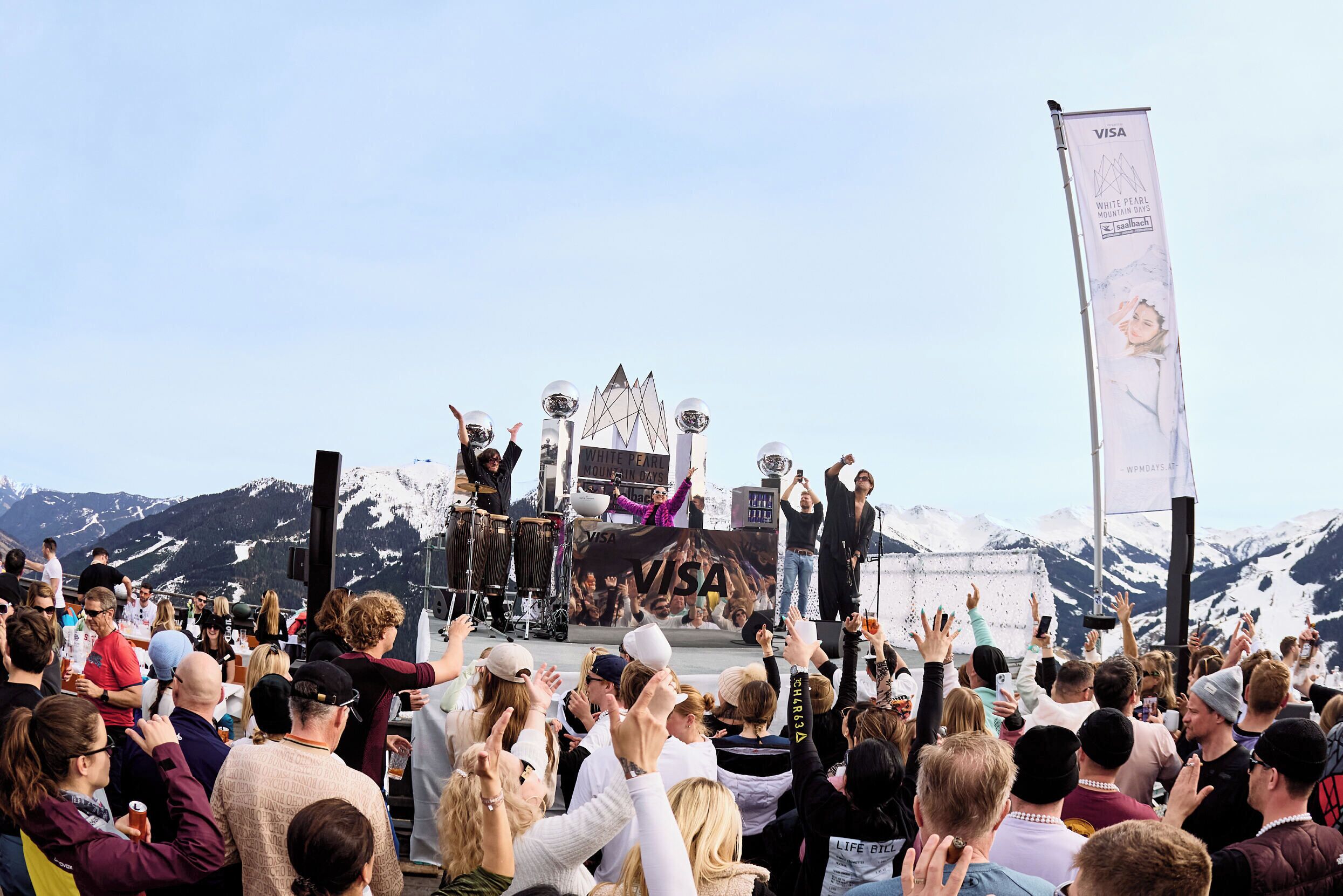 A stage with a crowd in front, a banner, and mountains in the background.