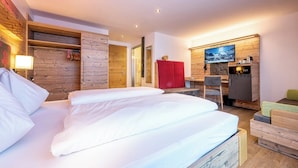A modern hotel room with a wooden wall, a bed with white linens, a red cabinet, a television, and a small seating area. - Siegmundshof Hotel Garni (Saalbach)