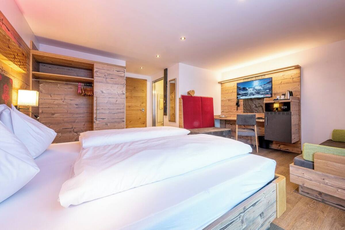 Ein modernes Hotelzimmer mit einer Holzwand, einem Bett mit weißen Leinen, einem roten Schrank, einem Fernseher und einer kleinen Sitzecke.