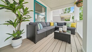 A covered porch with a gray sectional sofa, wicker furniture, and a potted plant.