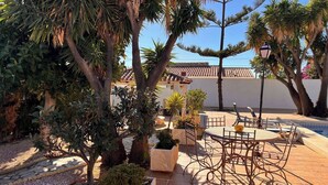 En udendørs patio med et rundt bord og stole, omgivet af krukker med planter og træer.
