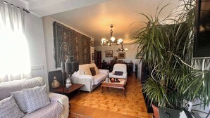 En hyggelig stue med sofa, lænestol og sofabord, et mønstret vægophæng og en stor plante.