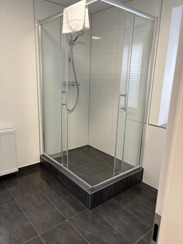 A glass-enclosed shower room with a white towel hanging on the door.