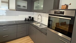 A modern kitchen with grey cabinets, a stainless steel range hood, a built-in oven, and a wooden floor. - Super nice and extremely large apartment approx. 145 m² in a country house in Priorei (Hagen)