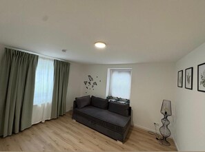 A living room with a grey sofa, a window with blinds, a floor lamp, and wall art.