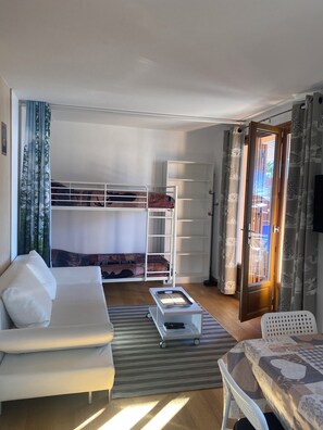A room with a bunk bed, a sofa, a small table, and a chair.