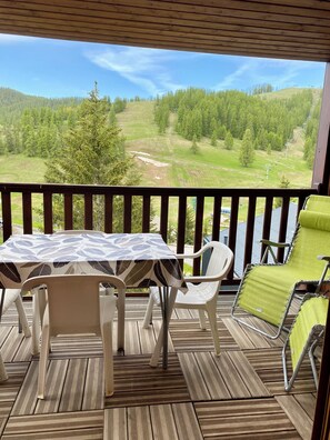 Una terraza de madera con una mesa y sillas, con vista a un paisaje verde con árboles y una colina.