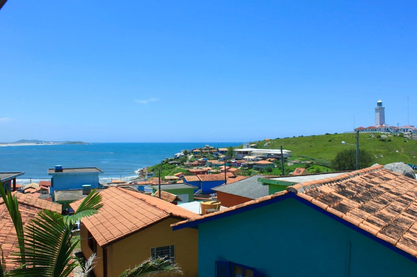 Uma vila costeira com um farol, edifícios com telhados de terracota e vista para o mar.