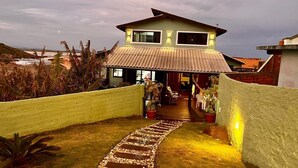 A house with a paved pathway leading to the entrance, surrounded by plants and a view of the ocean. - Chalés Santa Marta (Laguna)